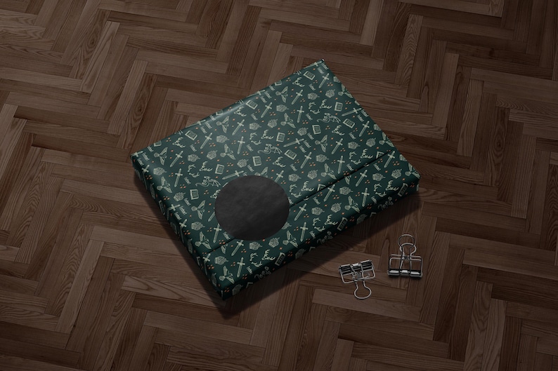 A green and gold patterned gift box with a black circular design on the front, placed on a wooden floor.