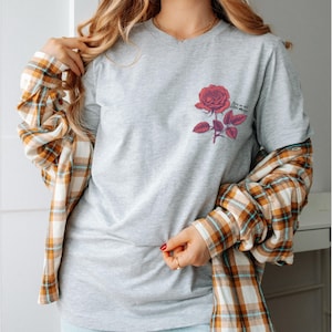 a woman wearing a grey shirt with a rose on it