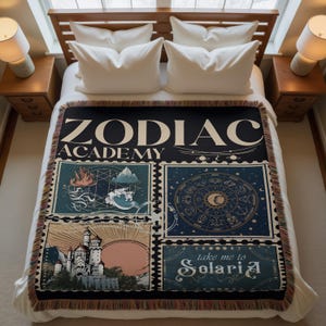 May include: A black woven throw blanket with the words "ZODIAC ACADEMY" in cream-colored text. The blanket features four illustrated panels with celestial and fantasy themes, including a zodiac wheel and a castle scene. The blanket has a fringed edge.