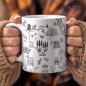A person's hands holding a white mug with various black and white illustrations and text on it.