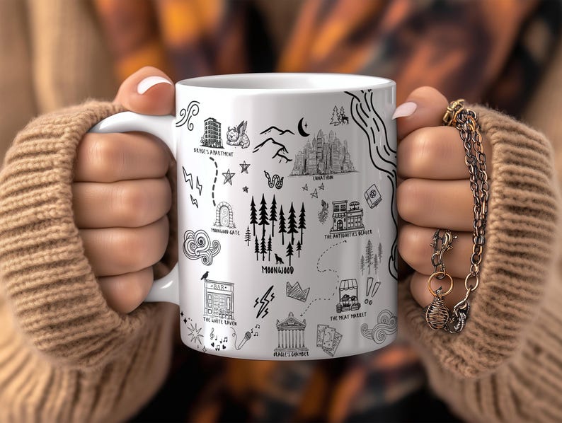 A person's hands holding a white mug with various black and white illustrations and text on it.