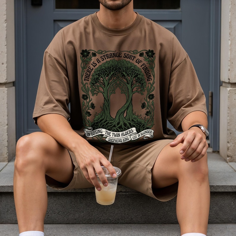 Brown t-shirt with "The Twin Alders" design, featuring trees and text.
