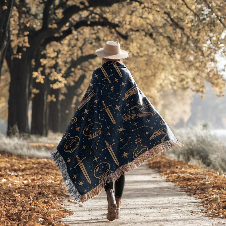 A woman walks down a path in a park, wearing a blue blanket with a starry pattern and a wide-brimmed hat.