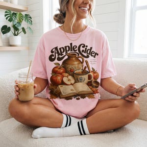 Pink t-shirt with "Apple Cider a crisp autumn classic" graphic and autumn details.