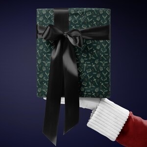 A gift wrapped in green paper with a black ribbon, held by a hand wearing a red glove against a dark blue background.