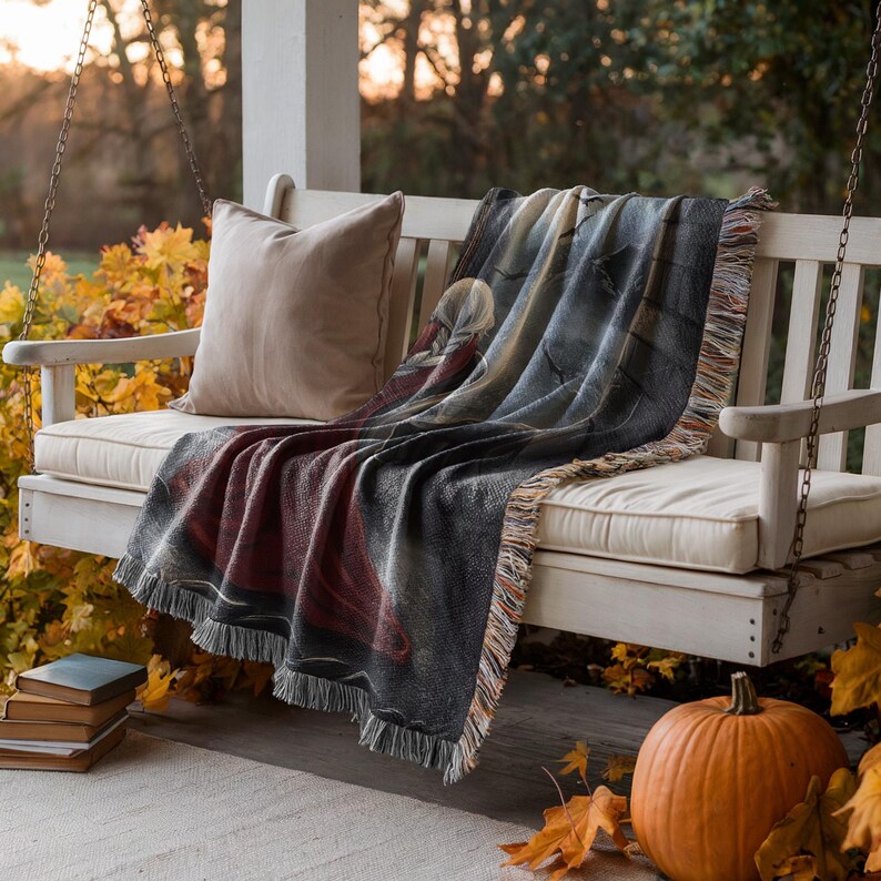 a cozy porch scene with a white wooden bench, a colorful throw blanket, a single pillow, and a pumpkin. The bench is situated on a porch with a swing, and the porch is surrounded by autumn leaves.