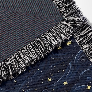 May include: Woven throw blanket with a dark teal and burgundy textured top side and a navy blue side with a starry night design. The blanket has a white and black fringe.