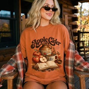 Orange t-shirt with "Apple Cider" graphic featuring apples, a jug, and a book.