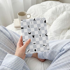 May include: A gray and white checkered notebook featuring various black illustrations, including a rose, butterfly, and crown. The notebook is held by a person wearing blue and white striped pajamas.