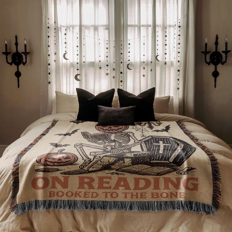 a bedroom with a bed covered in a blanket featuring a skeleton and bats, along with a Halloween-themed design. The bed is positioned in front of a window with curtains and string lights hanging from it.