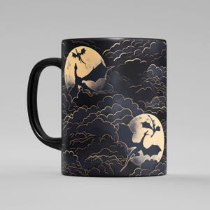 Op de afbeelding: Zwarte keramische mok met een fantasieontwerp. De mok heeft een herhalend patroon van silhouetten van draken tegen een volle maan en wolken. De handgreep is zwart en het ontwerp heeft gouden accenten.