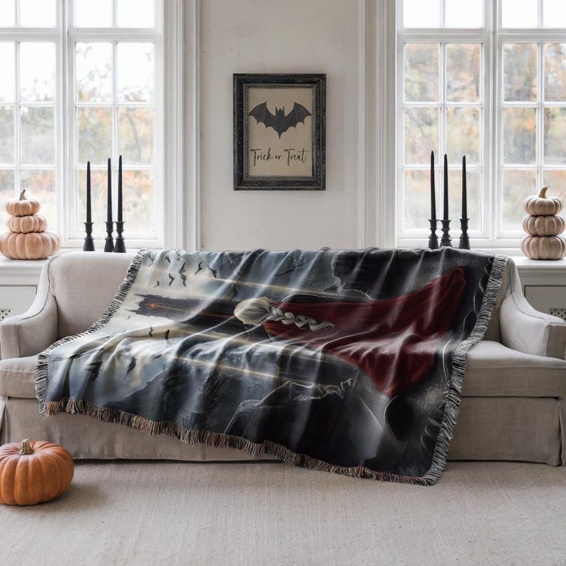 a living room with a large, colorful throw blanket on a couch, a framed Halloween-themed picture on the wall, and several candles on the windowsill.