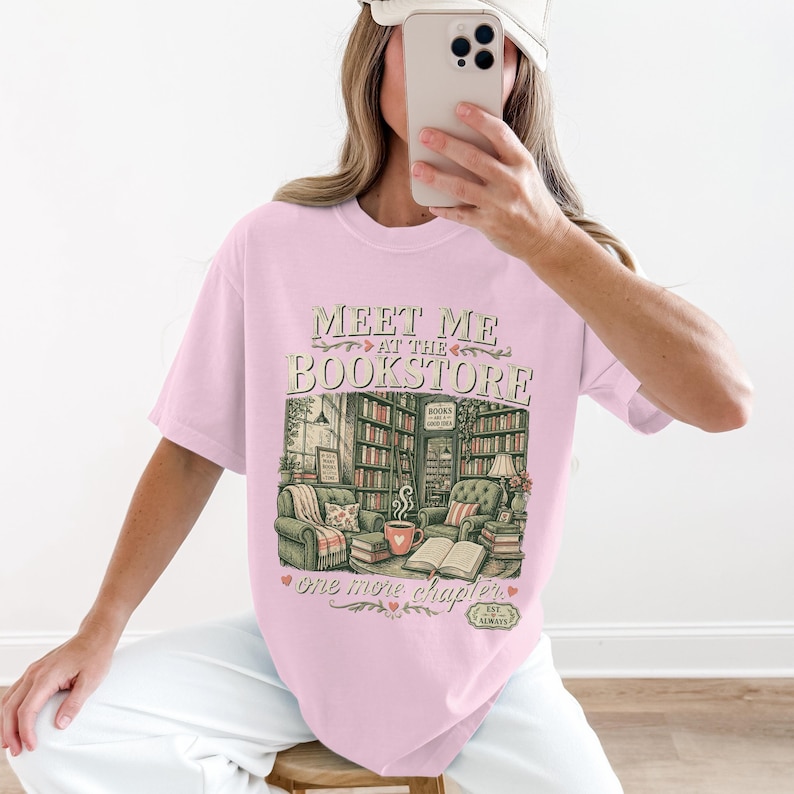 Pink t-shirt with "Meet Me at the Bookstore" graphic featuring a cozy room.