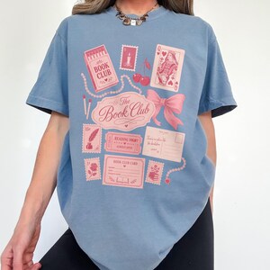 Blue t-shirt with pink "The Book Club" graphic featuring stamps, cards, and cherries.