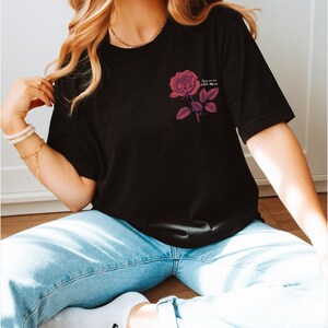 a woman sitting on the floor wearing a t - shirt with a rose on it