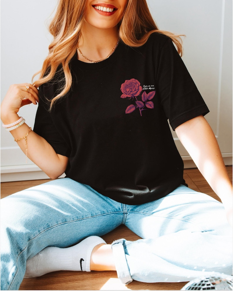 a woman sitting on the floor wearing a t - shirt with a rose on it