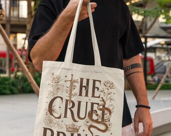 May include: Beige tote bag with the text "THE CRUEL PRINCE" in brown, featuring a sword, crown, and snake illustration. The design is surrounded by floral elements. The bag has long handles.