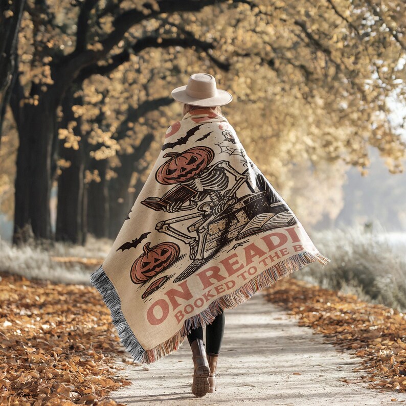 A person walking on a path in a forest, wearing a large blanket with a Halloween-themed design.