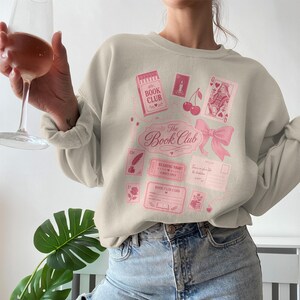 Light pink sweatshirt with book club themed graphics and text.