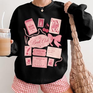 Black sweatshirt with pink book-themed graphics and text reading "The Book Club".