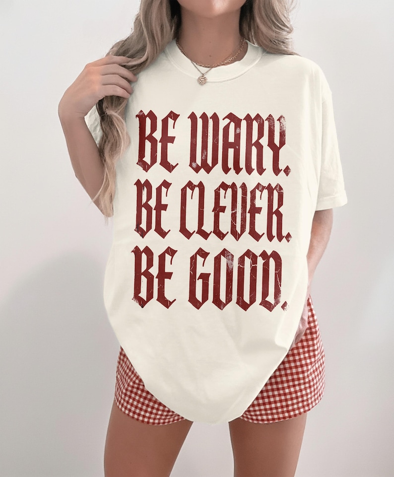 Cream t-shirt with red gothic text reading "Be Wary. Be Clever. Be Good."