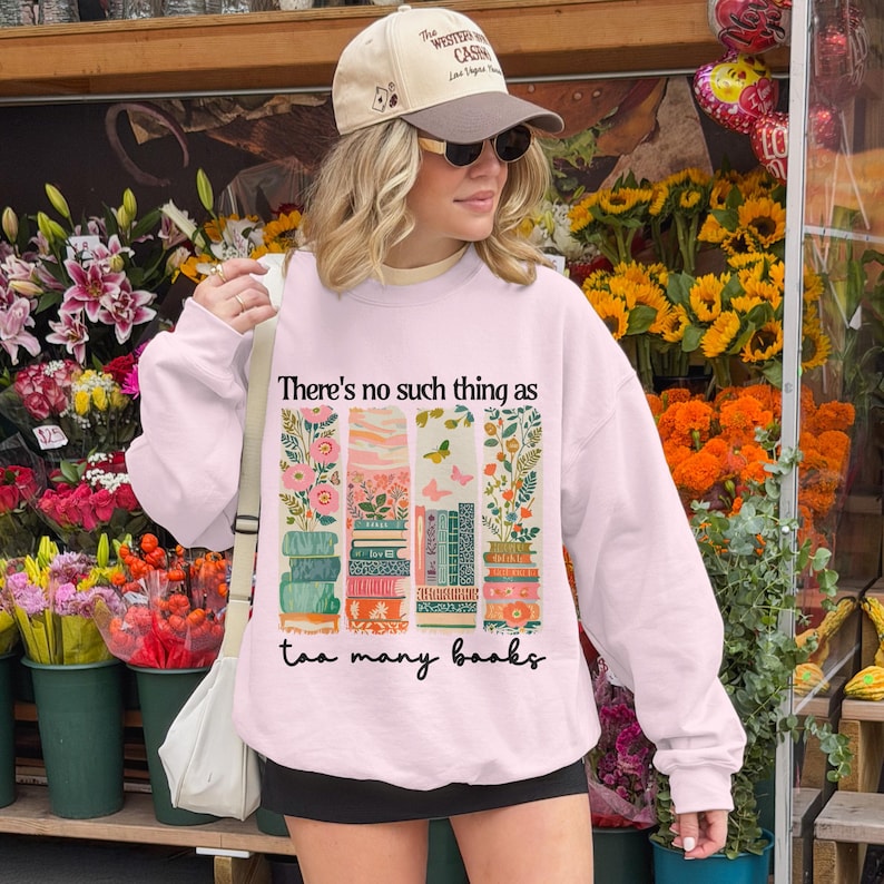 Light pink sweatshirt with books and floral design, reading "There's no such thing as too many books."