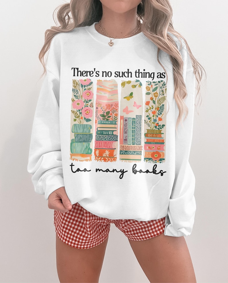 Sweatshirt with stacked books, floral patterns, and the phrase "There's no such thing as too many books."