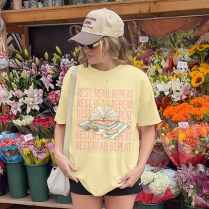 Woman in tan cap wearing t-shirt with "REST, READ, REPEAT" text.