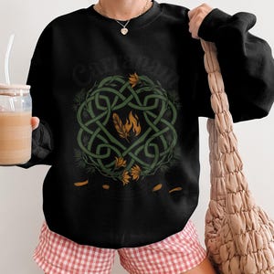 Black crewneck sweatshirt with Celtic knot design and feather emblem.
