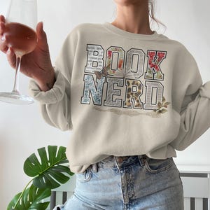 Cream sweatshirt with "BOOK NERD" text in a collage of floral and book page patterns.