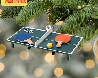 May include: A Christmas tree decoration in the shape of a table tennis table. The ornament features a green surface, a white net, two bats, and a yellow ball. The word "NAME" is printed on the table. It hangs from a gold chain. The text "PERSONALIZED DESIGN CUSTOM TEXT & IMAGE" is printed on a yellow rectangle.