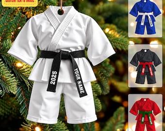 May include: A white martial arts uniform ornament featuring a black belt with the text 2025 and YOUR NAME printed on it. The ornament includes a gold hanging string. Additional color variations of blue, black, and red uniforms are shown.