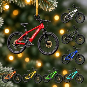 Puede incluir: Un adorno colgante con forma de bicicleta de montaña con cuadro rojo, neumáticos negros y frenos de disco dorados. El cuadro presenta el texto YOUR NAME en blanco. Se muestran versiones más pequeñas de la bicicleta en blanco, negro, azul, naranja, amarillo, verde y turquesa.