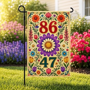 Può includere: Una bandiera da giardino decorativa con un design floreale e i numeri 86 e 47. La bandiera ha uno sfondo color crema con fiori arancioni, viola, blu e gialli. I numeri sono rossi e verde acqua.