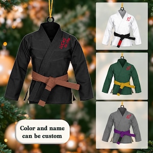 Può includere: Un ornamento da appendere a forma di gi per arti marziali con cintura. Il gi principale è nero con cintura marrone e scritta rossa Lucas Jiu Jitsu. Altre versioni mostrano un gi bianco, verde o grigio con le rispettive cinture colorate.