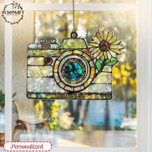 Peut inclure: Une décoration de caméra en vitrail avec un motif de tournesol. L'appareil photo est iridescent et a un bijou bleu dans l'objectif. L'ornement a le texte "Custom Text" en bas.
