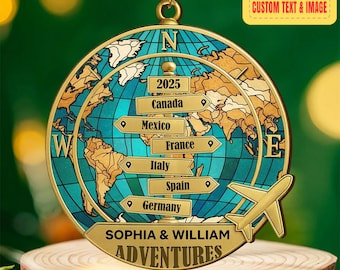May include: A round, gold-colored travel-themed ornament with a world map design. The ornament features a teal blue ocean, tan continents, and directional signs pointing to various countries. Text includes "2025", "Canada", "Mexico", "France", "Italy", "Spain", "Germany", and "SOPHIA & WILLIAM ADVENTURES".