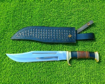 May include: A silver and brown hunting knife with a leather sheath. The knife has a long, sharp blade and a wooden handle.