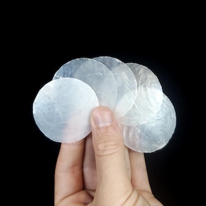 May include: A collection of six iridescent white mother of pearl shell discs, held in a hand.