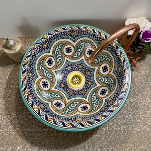 Puede incluir: Un lavabo de cerámica con un diseño estampado en verde, azul y amarillo. El lavabo tiene un grifo de cobre.