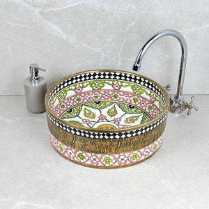 May include: A round ceramic sink with a colourful floral pattern in shades of pink, green, and white. The sink has a gold rim and a textured gold base.