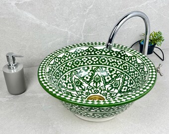 May include: A decorative, round ceramic sink with a green and white floral pattern. A silver faucet and soap dispenser are next to the sink. The sink is a vessel style, and the overall design is ornate.
