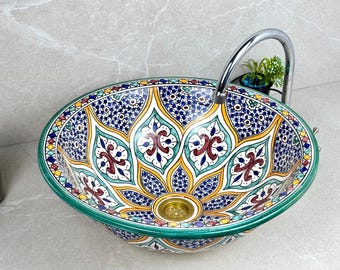 May include: An oval ceramic sink with a vibrant, intricate floral pattern in blue, yellow, red, and green. The sink has a gold drain and a green border. A chrome faucet is installed above the sink.