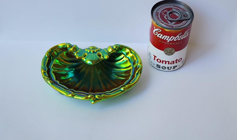 Peut inclure: Un plat en forme de coquillage avec une finition iris&eacute;e verte et dor&eacute;e, dot&eacute; d'un bord festonn&eacute; et d'un motif d&eacute;coratif central. &Agrave; c&ocirc;t&eacute; du plat se trouve une bo&icirc;te de soupe &agrave; la tomate Campbell's de 305g pour montrer l'&eacute;chelle de taille.