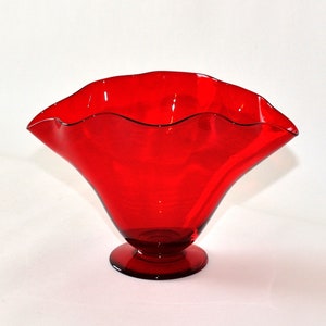 May include: A red glass vase with a ruffled rim and a flared base. The vase is made of clear glass with a red tint.