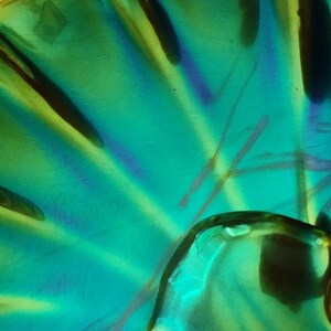 Peut inclure: Un plat en verre iris&eacute; vibrant pr&eacute;sentant un motif radial en &eacute;ventail. La surface affiche un &eacute;clat m&eacute;tallique avec des teintes changeantes de vert &eacute;meraude, de bleu sarcelle et des reflets violets, cr&eacute;ant une finition brillante et r&eacute;fl&eacute;chissante.