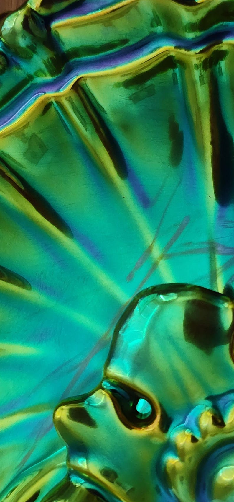 Peut inclure: Un plat en verre iris&eacute; vibrant pr&eacute;sentant un motif radial en &eacute;ventail. La surface affiche un &eacute;clat m&eacute;tallique avec des teintes changeantes de vert &eacute;meraude, de bleu sarcelle et des reflets violets, cr&eacute;ant une finition brillante et r&eacute;fl&eacute;chissante.