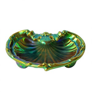 Peut inclure: Un plat en forme de coquillage avec une finition iris&eacute;e aux reflets m&eacute;talliques verts, dor&eacute;s et bleu profond. Le bol pr&eacute;sente un bord festonn&eacute;, un motif d&eacute;coratif central et repose sur trois petits pieds arrondis &agrave; la base.