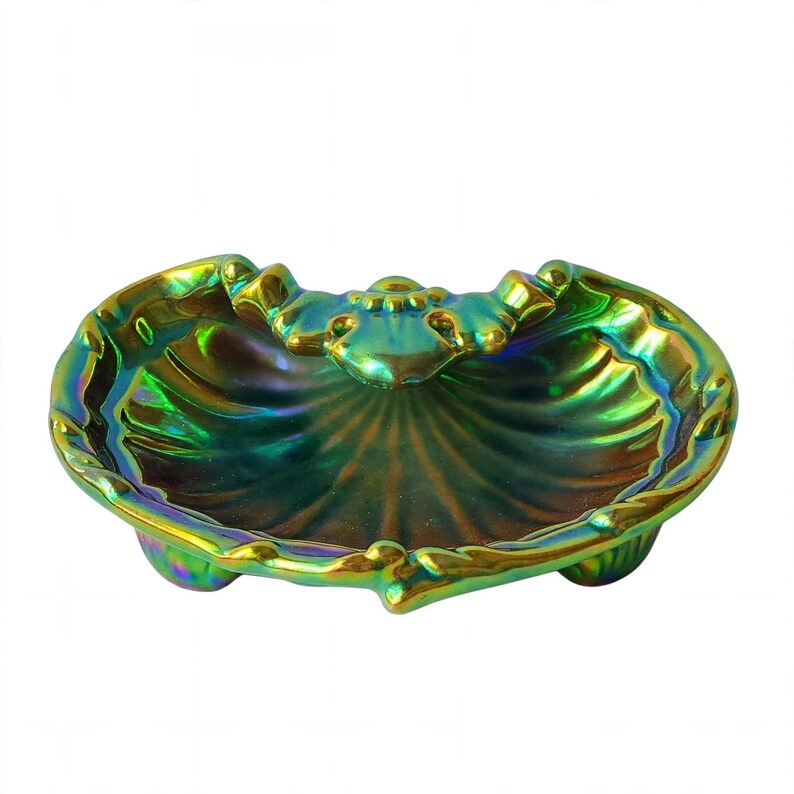 Peut inclure: Un plat en forme de coquillage avec une finition iris&eacute;e aux reflets m&eacute;talliques verts, dor&eacute;s et bleu profond. Le bol pr&eacute;sente un bord festonn&eacute;, un motif d&eacute;coratif central et repose sur trois petits pieds arrondis &agrave; la base.