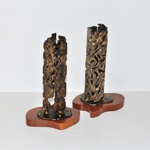 May include: Two abstract metal sculptures with a textured, gold-like finish, mounted on wooden bases. The sculptures are tall and narrow, with a unique, organic design.